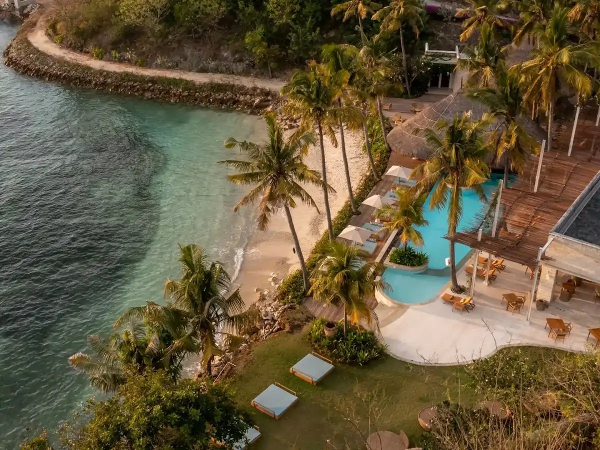 Aerial view of the white-sand cove, pool and thatched pavilions of Silo Beach Club at Semaya on Nusa Penida, Bali