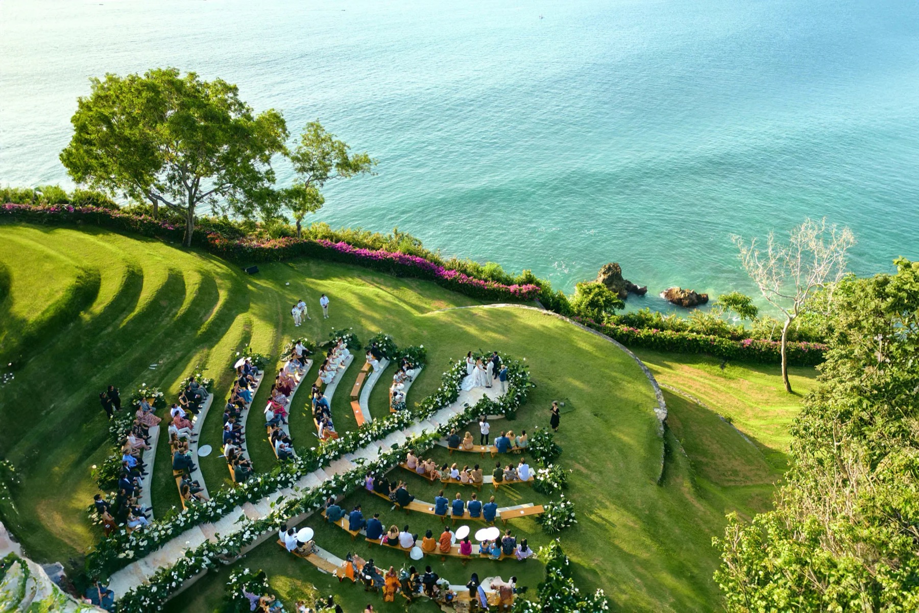 Aerial view of a wedding ceremony on a curved grass terrace at SKY, AYANA, set high on the cliff above the turquoise Indian Ocean