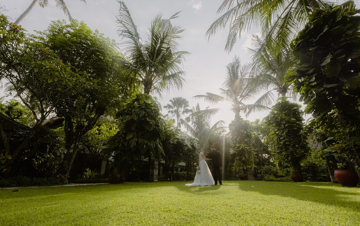 Couple standing on the palm-shaded lawn in the afternoon sun at Sudamala Resort, Senggigi on Lombok's west coast