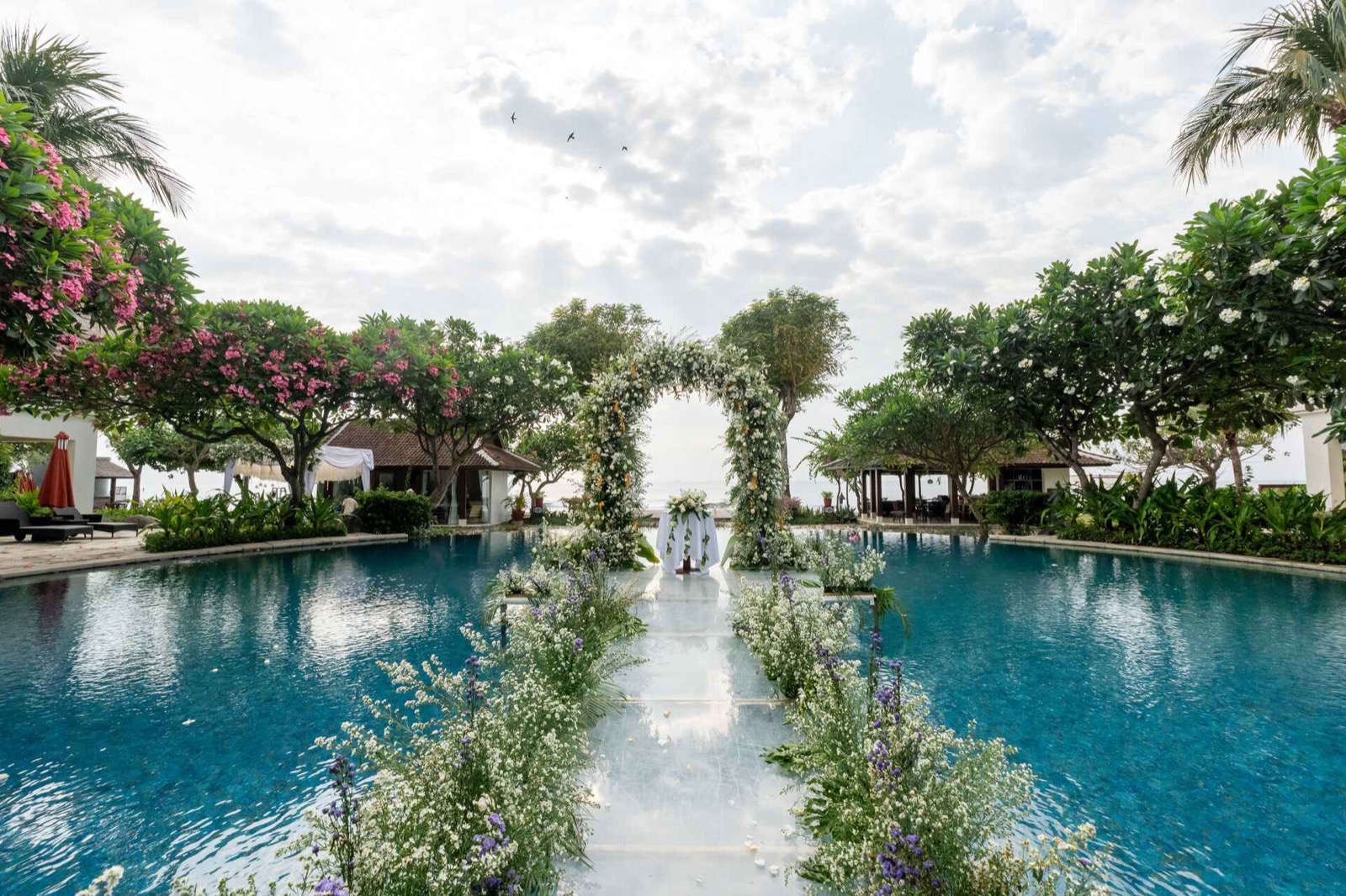 Wedding aisle laid across the swimming pool to a floral arch facing the sea at Sudamala Resort, Senggigi, Lombok