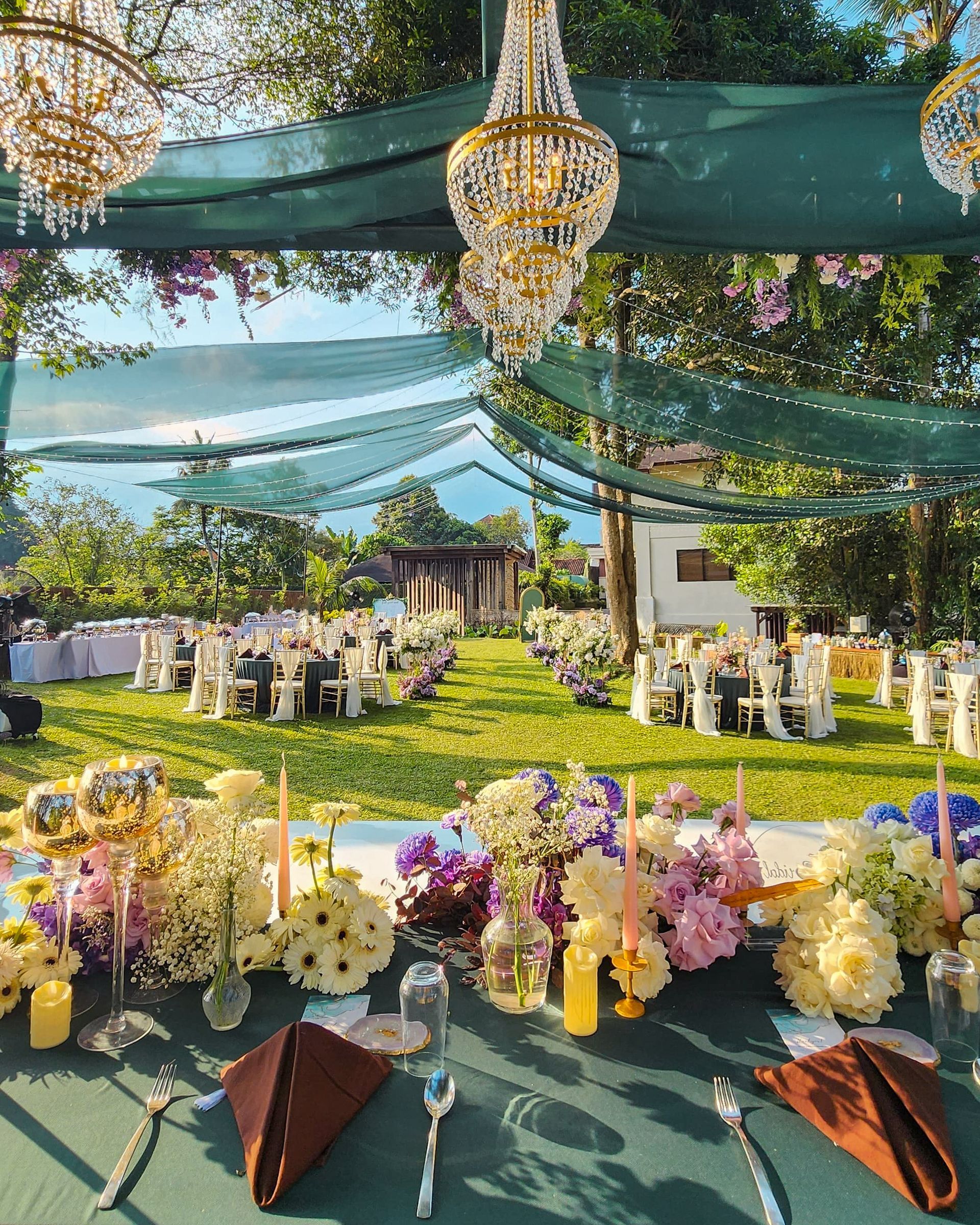 Outdoor wedding reception beneath green canopy with pink flowers and chairs at Tanadewa Resort