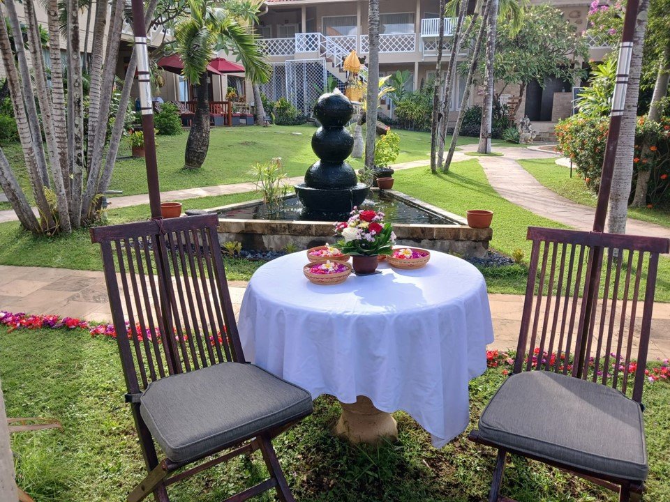 Table for two laid with flower petals and offerings beside the garden fountain at Tauch Terminal Resort Tulamben & Spa in northeast Bali