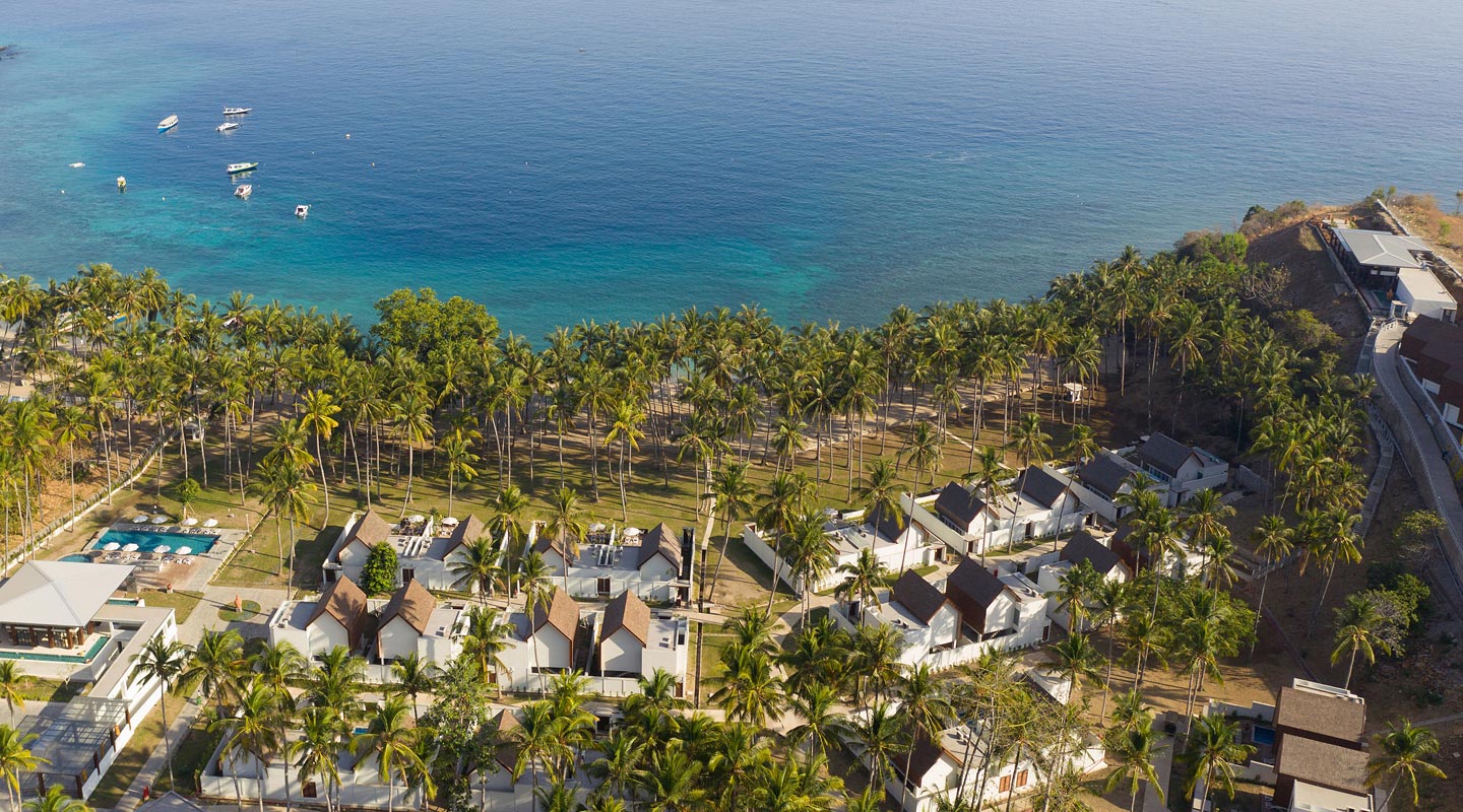 Aerial view of the white villas among coconut palms above the turquoise bay at The Kayana Beach Lombok
