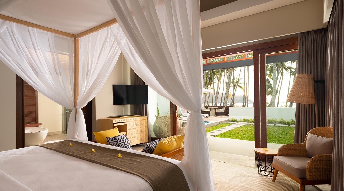 Villa bedroom with a canopy bed opening onto a private garden and the beach at The Kayana Beach Lombok