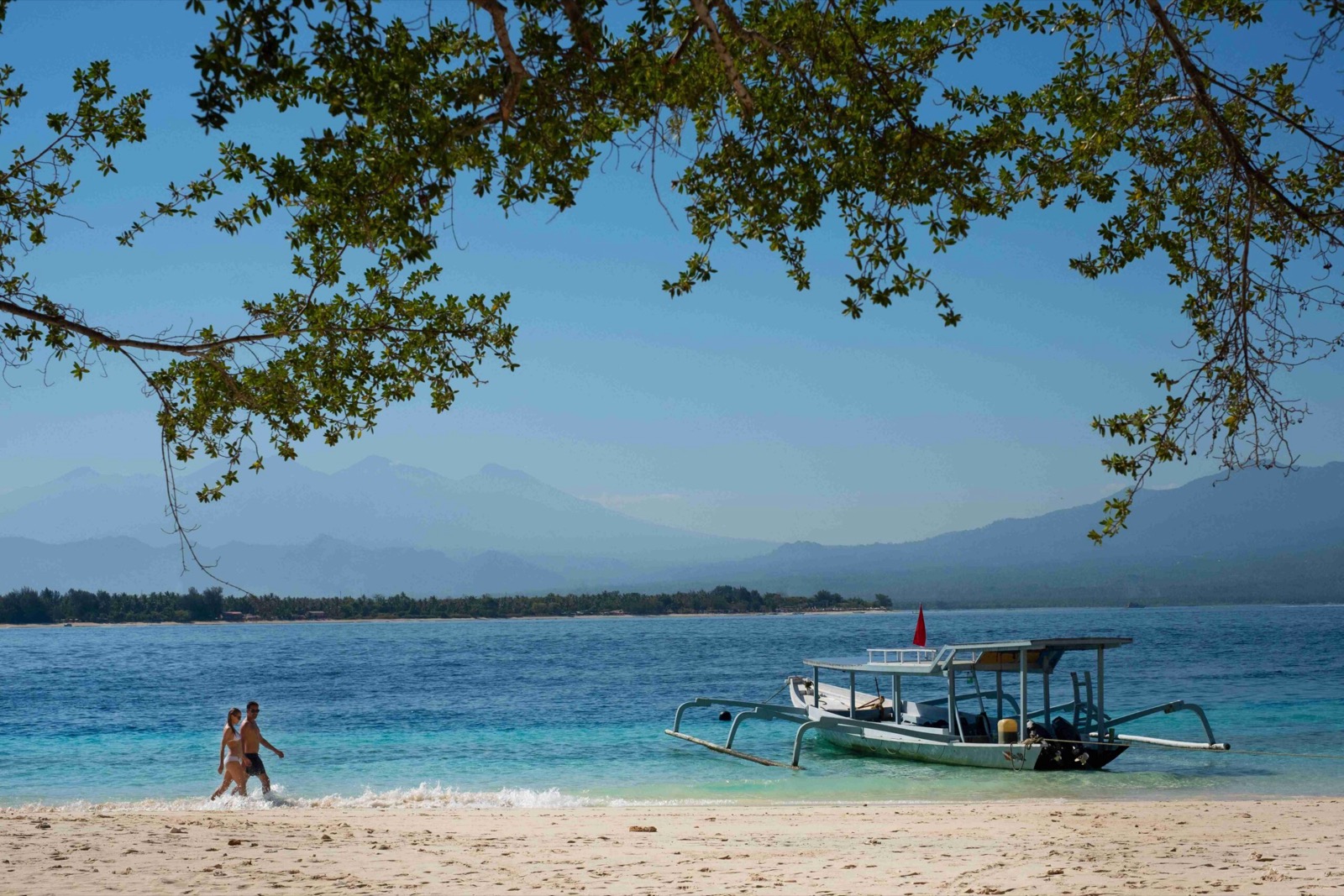 White sand, an outrigger boat and Mount Rinjani across the water on the Gili crossing near The Kayana Beach Lombok