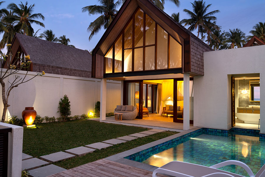 Pool villa with a gabled glass facade lit at dusk at The Kayana Beach Lombok