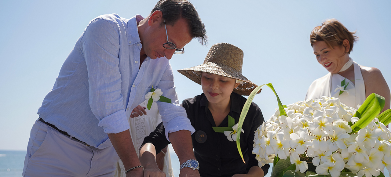 Couple signing the ceremony certificate beside a staff member and a bowl of frangipani at The Lombok Lodge on Lombok's northwest coast