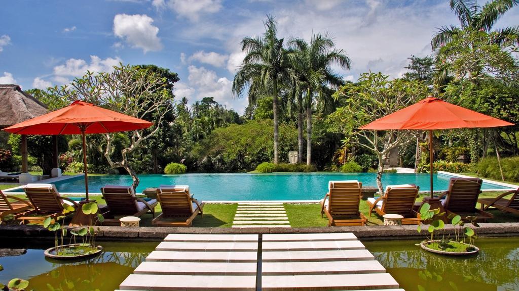 Pool deck with orange umbrellas and wooden daybeds at The Lotus Residence, framed by palm trees