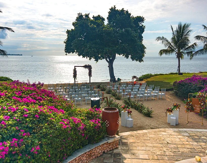 Ceremony chairs and floral plinths arranged around a tree at the water's edge at sunset, The Oberoi Beach Resort Lombok, Tanjung