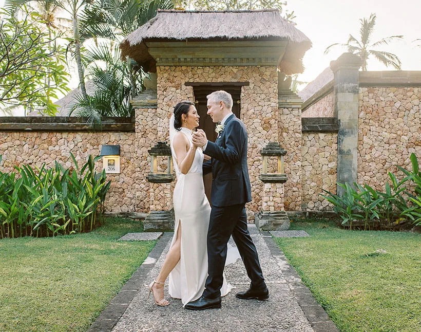 Couple dancing on the lawn in front of a thatched stone villa gateway at The Oberoi Beach Resort Lombok