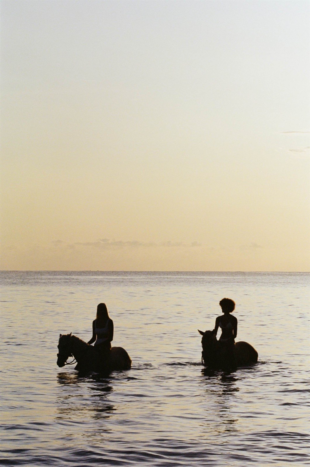 Two riders on horseback out in the sea at sunset in front of The Sanubari, Sumba