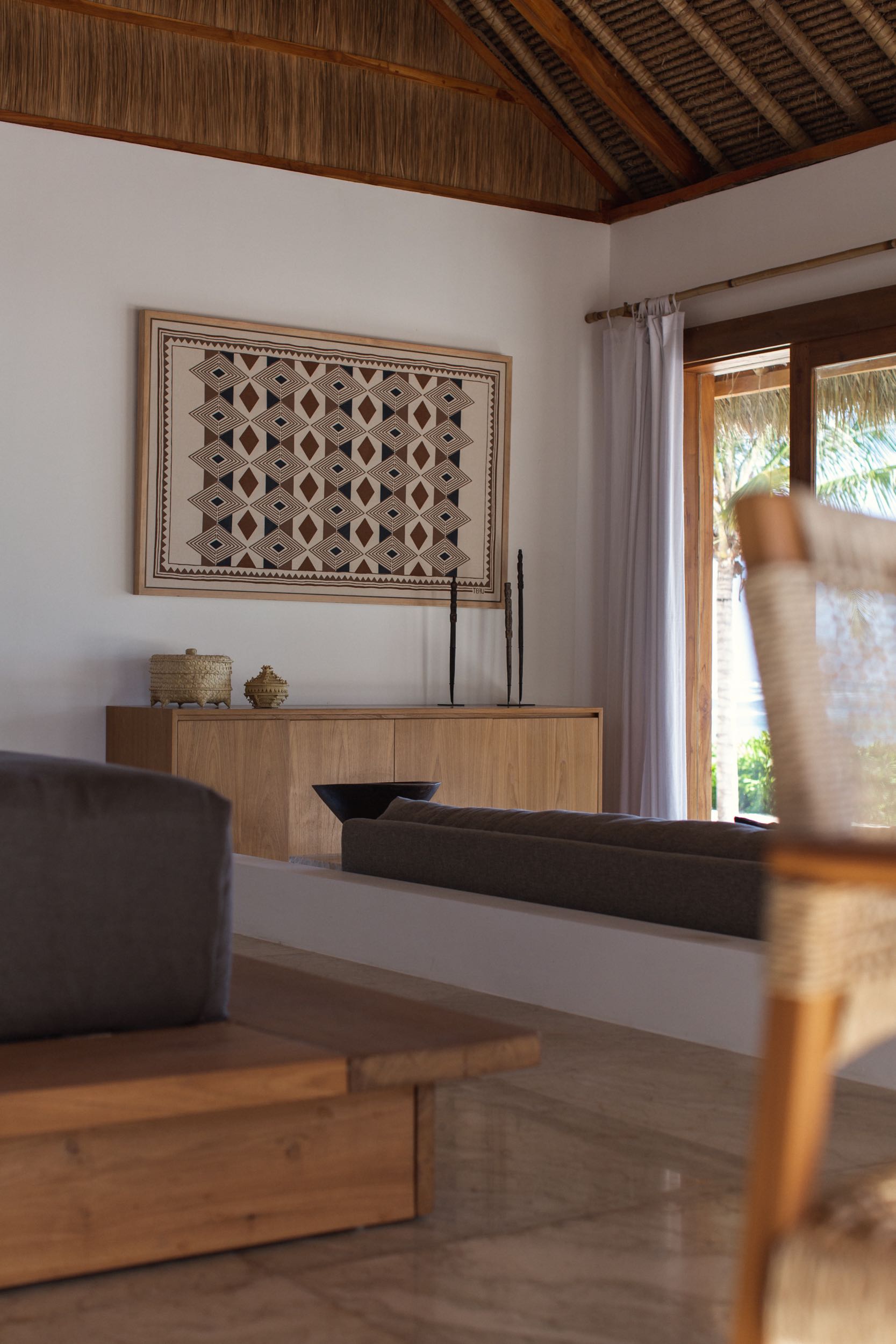 Villa living room under a thatched ceiling with a framed Sumbanese textile above the sideboard at The Sanubari, Sumba