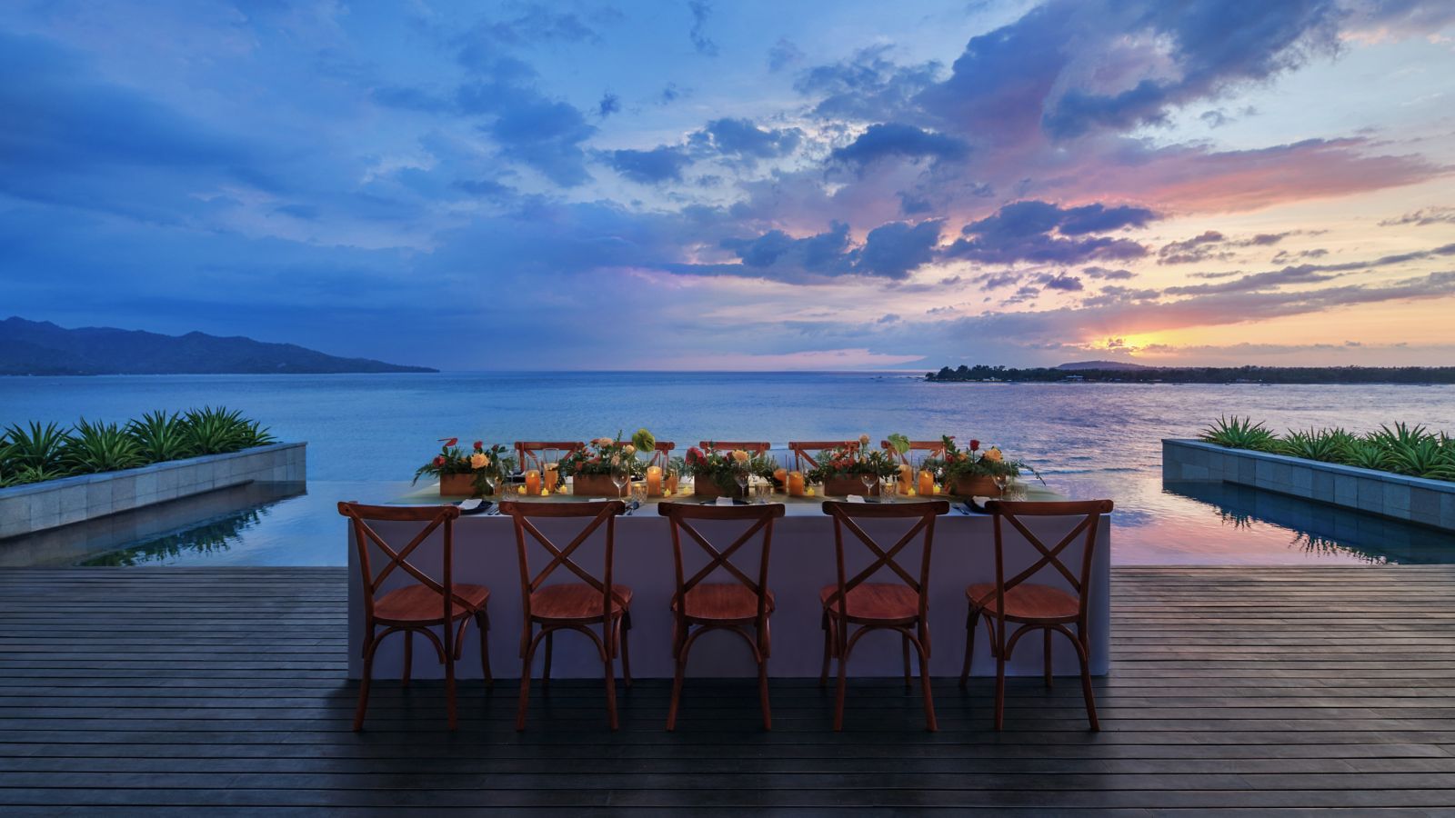 Long dinner table lit by candles on the ocean-edge deck at sunset at The Sira, Lombok