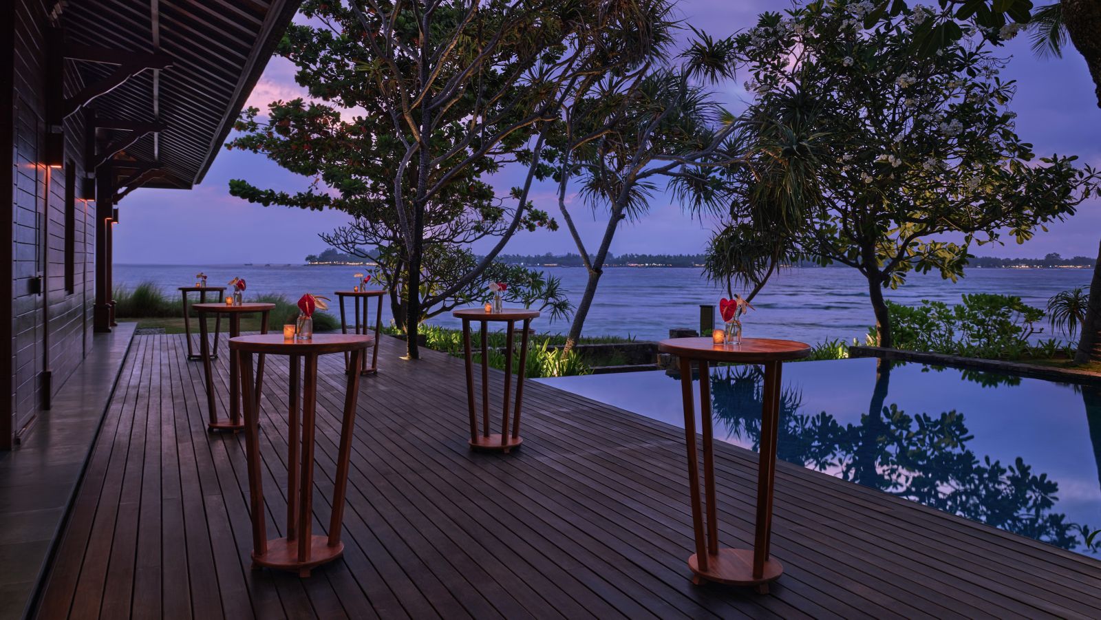 Cocktail tables set along the timber deck beside the pool at dusk at The Sira on Lombok