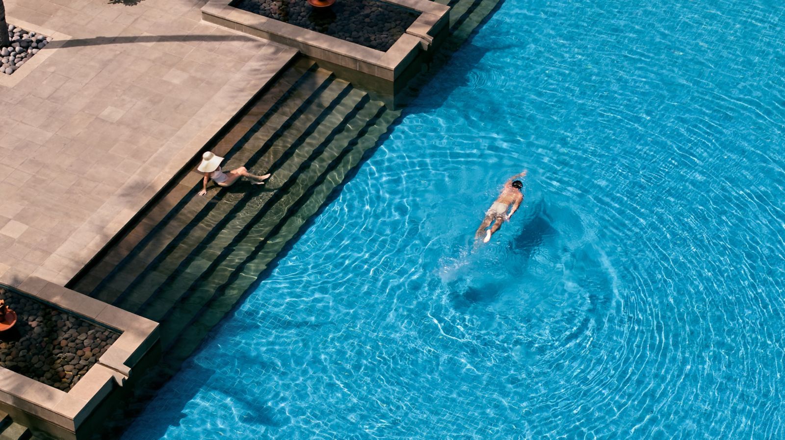 Swimmer crossing the resort pool beside its stone steps at The Sira, Lombok