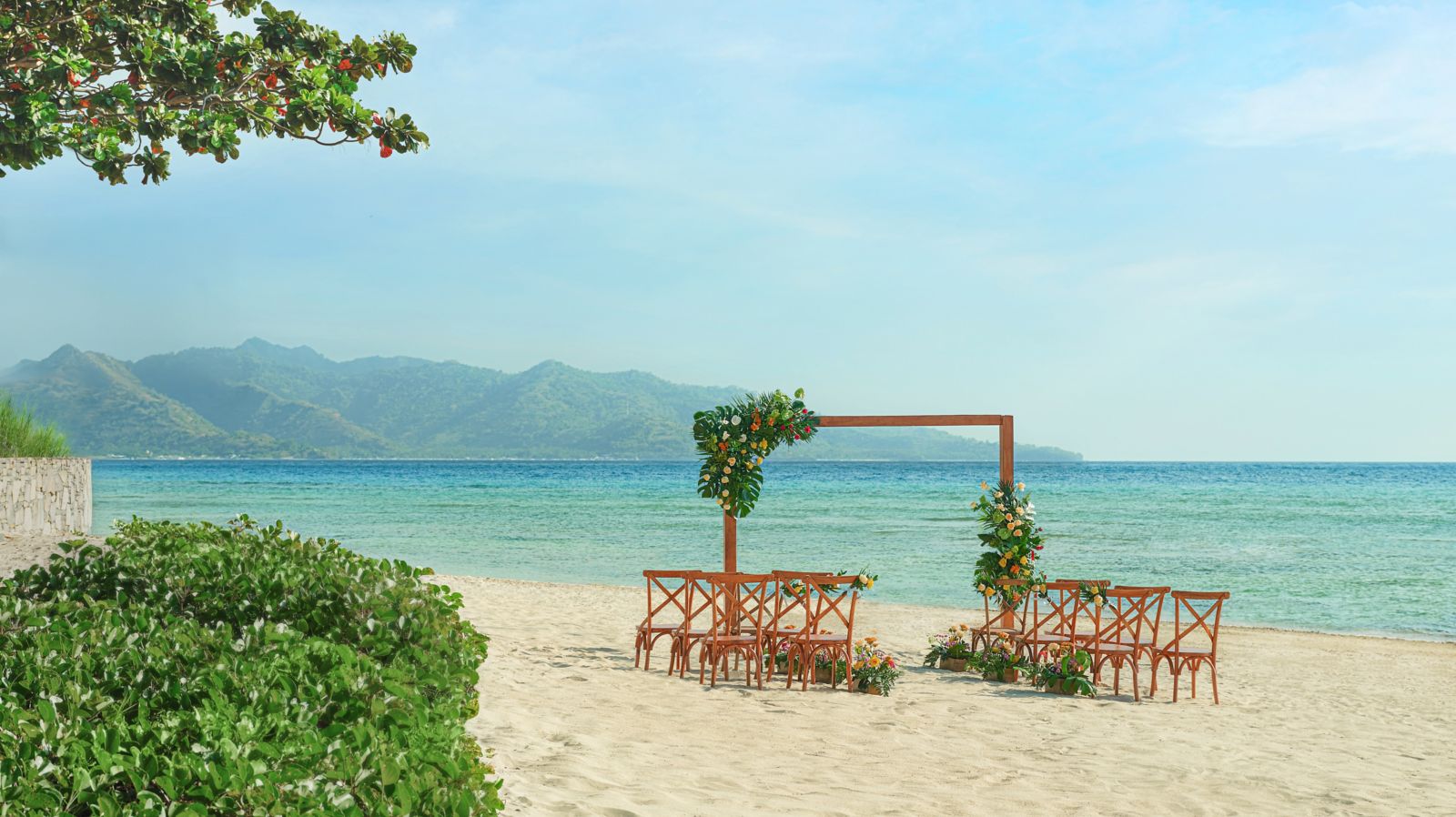Timber ceremony arch dressed with tropical flowers and wooden chairs on the white sand at The Sira, a Luxury Collection Resort and Spa, on Lombok's northwest coast