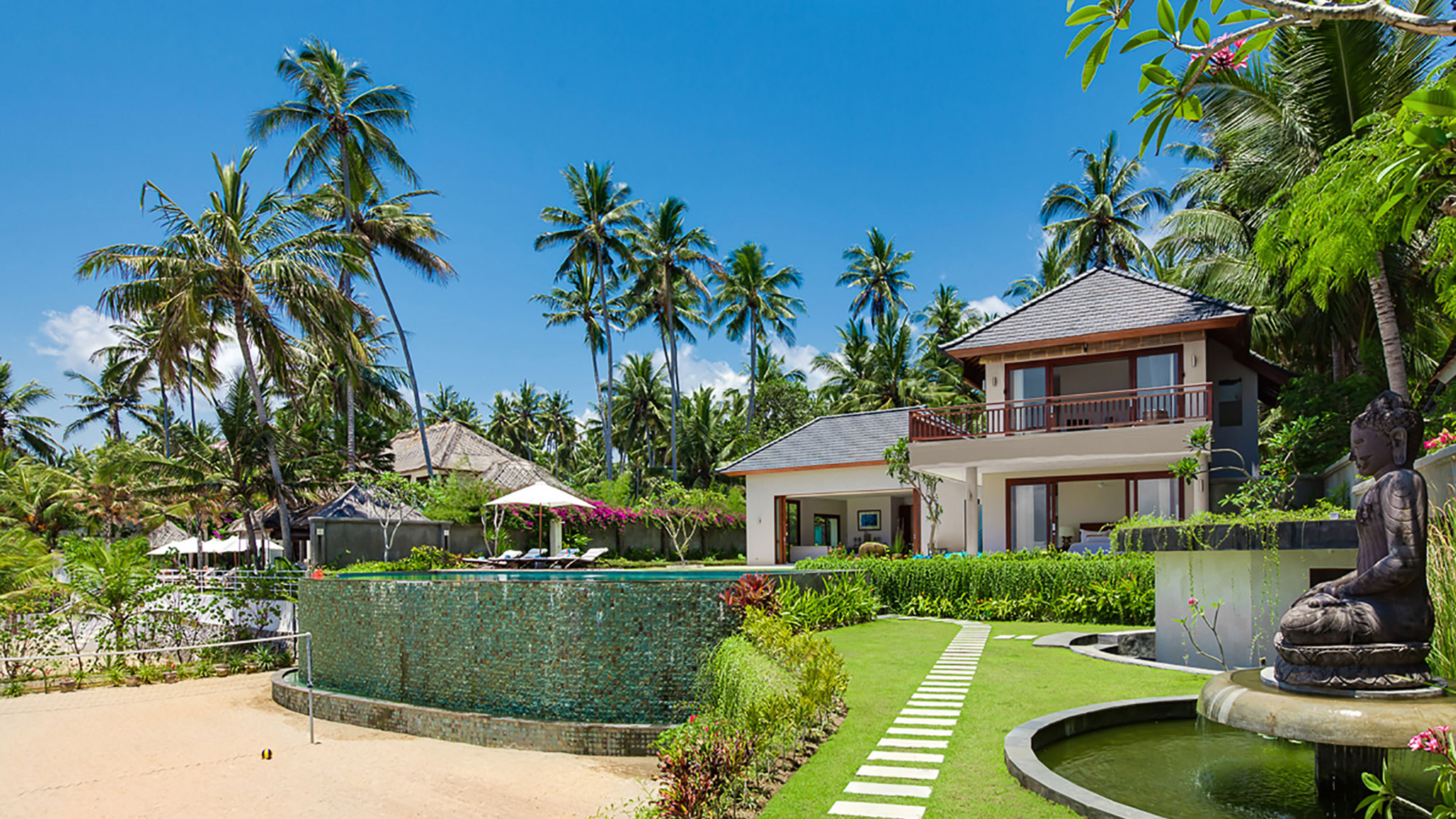 Pool and villa grounds at Tirta Nila with tropical gardens, palm trees, and beachfront setting