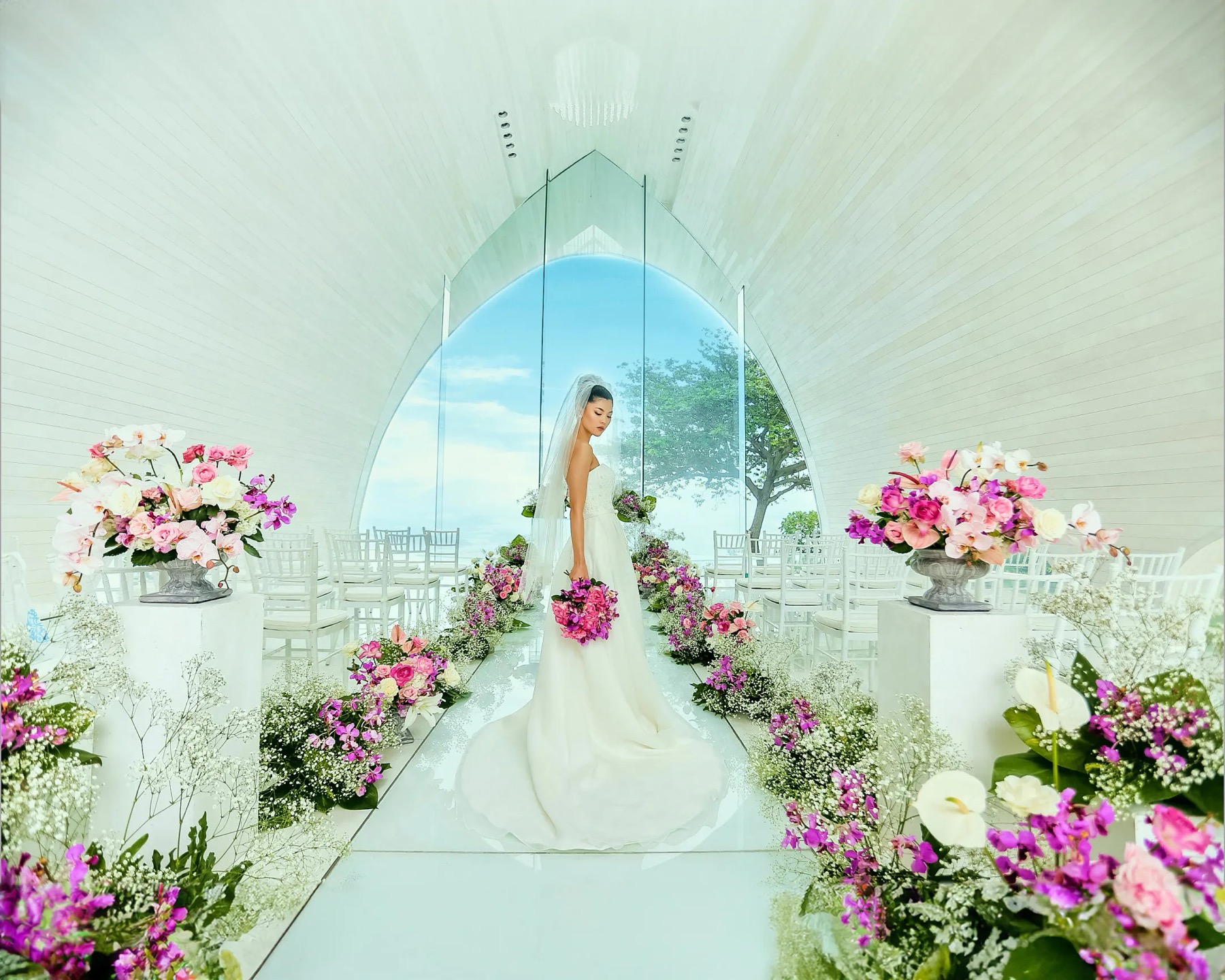 The white arched interior of Tresna Chapel at AYANA, with a glass wall behind the altar looking out to sky and ocean