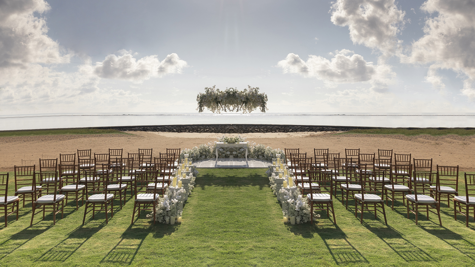 A ceremony set up on the beachfront lawn at The Royal Santrian in Tanjung Benoa, rows of chairs and a floral arch facing the Indian Ocean