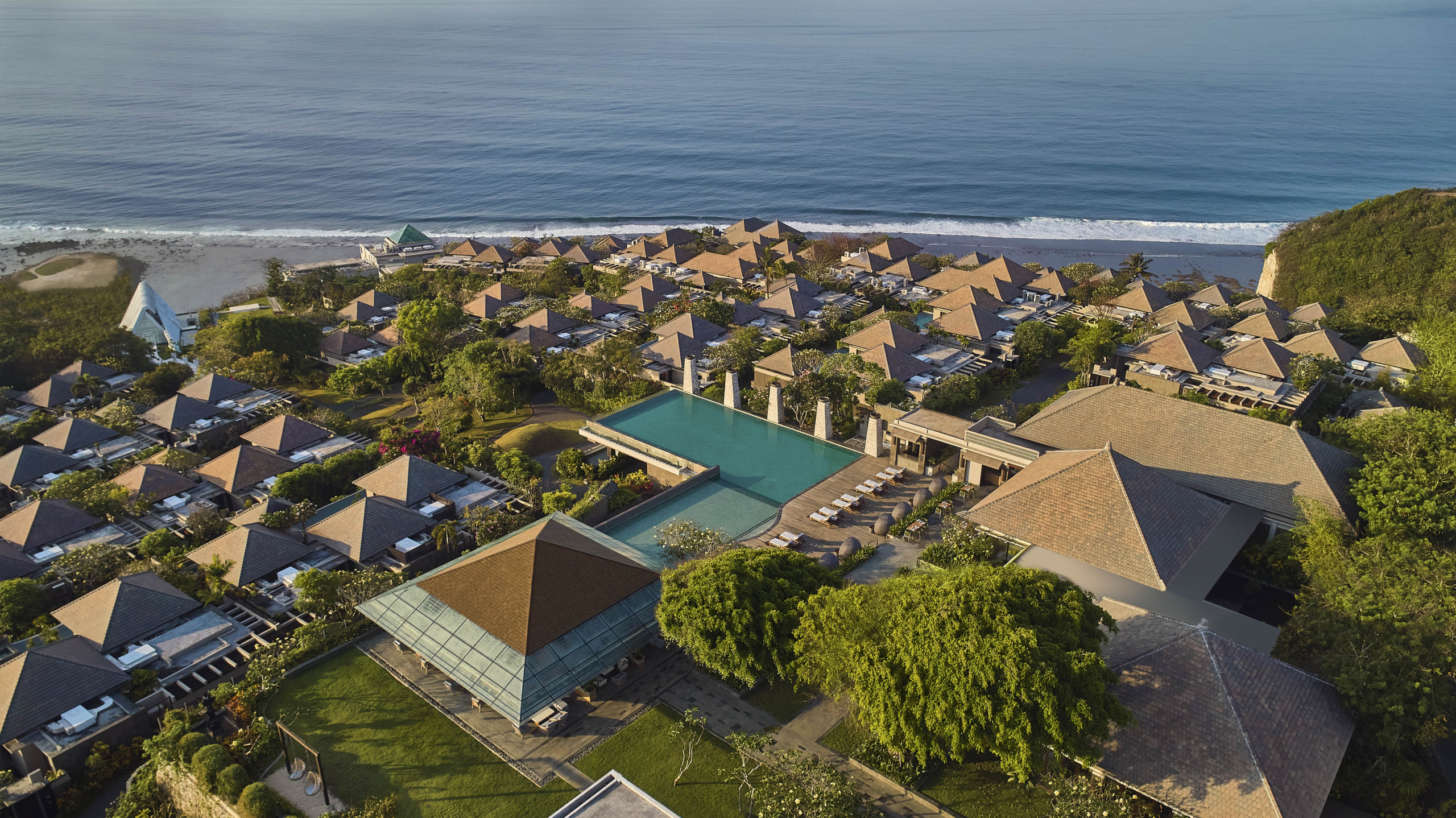 Cascading tiled-roof villas of UMANA Bali running down the cliff toward Melasti Beach and the ocean