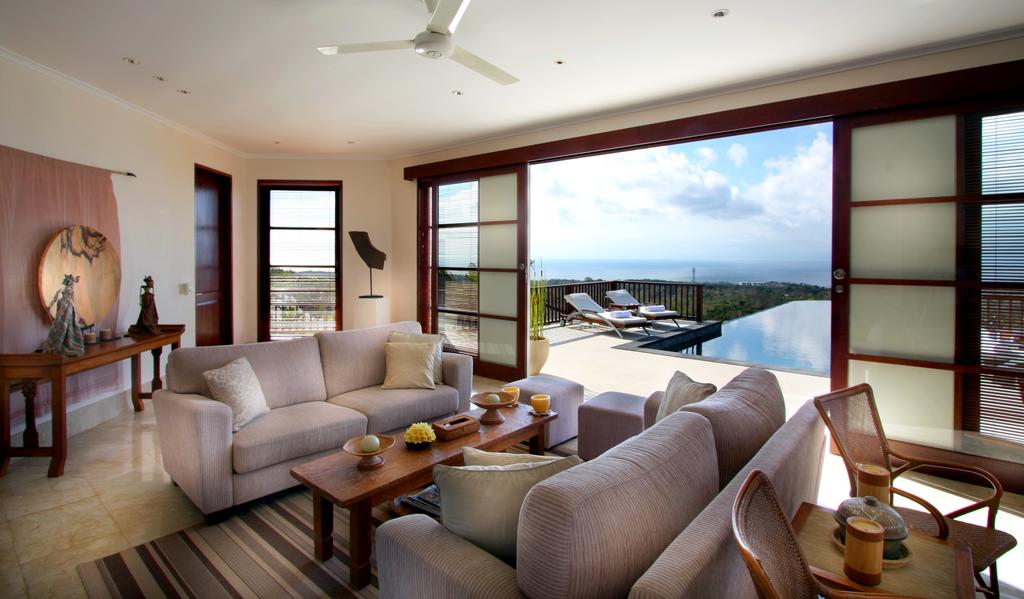Open-plan living room at Villa Ali Agung with sliding doors onto the pool terrace and an ocean view beyond