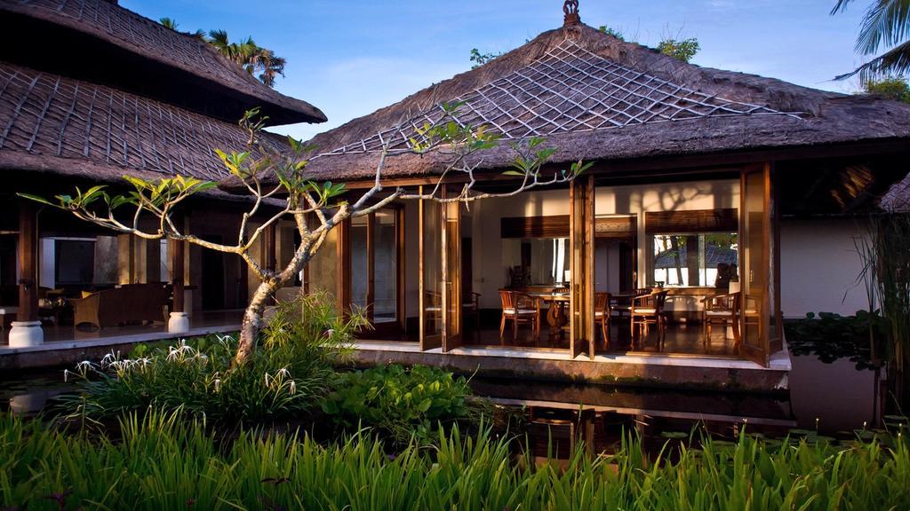 Villa Arika's thatched-roof pavilion and dining terrace at dusk, framed by a frangipani tree and a lily pond
