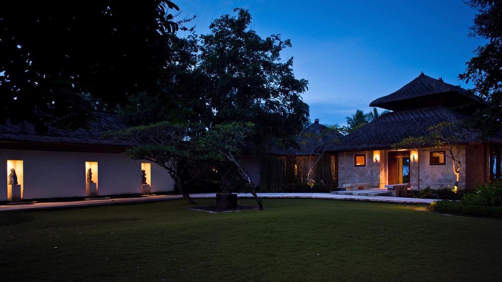 Villa Arika's garden courtyard at dusk, lined with stone statues and a lit walkway