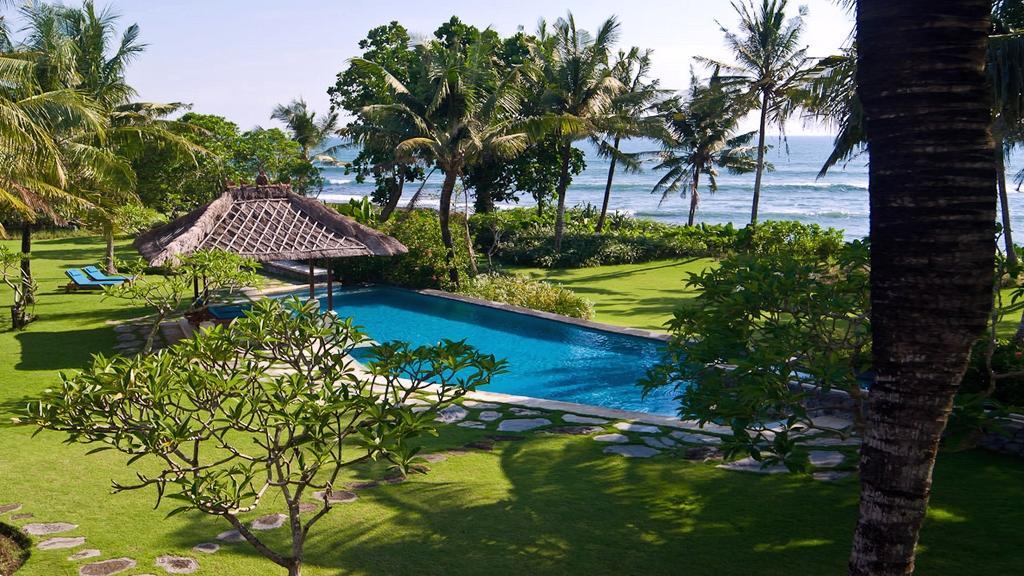 Infinity-edge swimming pool at Villa Arika in Canggu, Bali, with the ocean visible beyond the palm trees