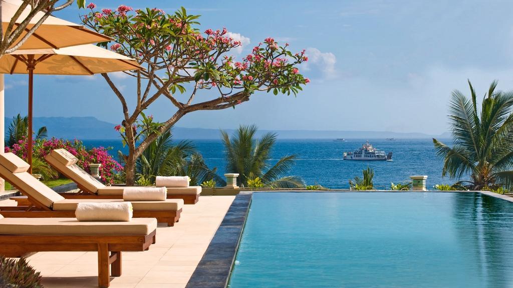 Sun loungers and frangipani tree beside the pool at Villa Asada, with a boat passing on the sea beyond