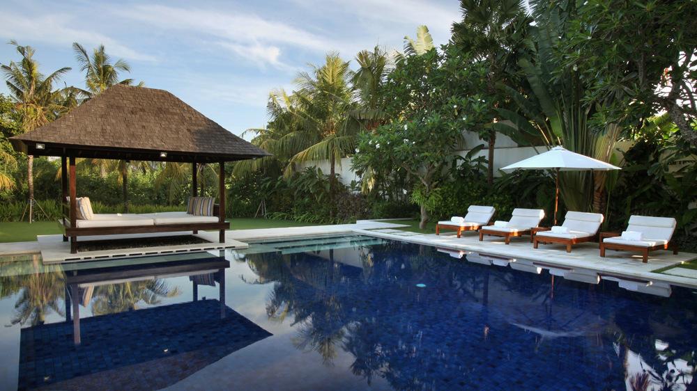 Thatched gazebo daybed and sun loungers beside the garden pool at Villa Asante