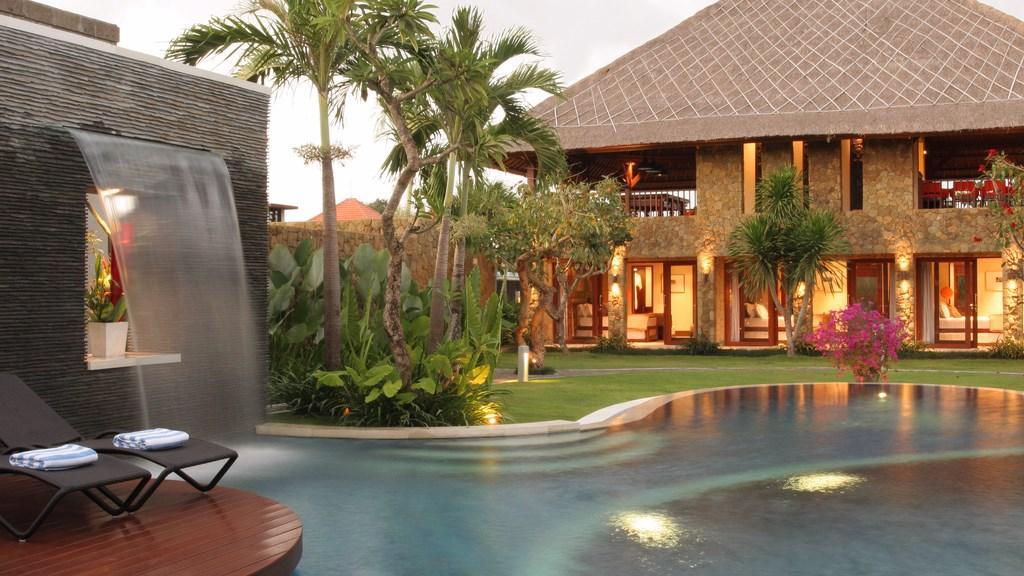 Villa Asta's stone water-wall pool deck by day, with the main house and gardens behind