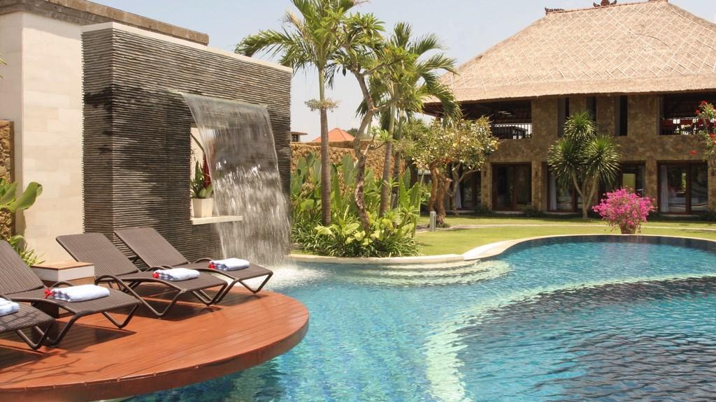 Poolside loungers beside the water feature at Villa Asta, with the villa's alang-alang roofline in view