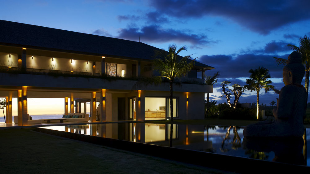 Villa Babar lit at dusk, the reflecting pool and garden with the ocean behind on the Tabanan headland