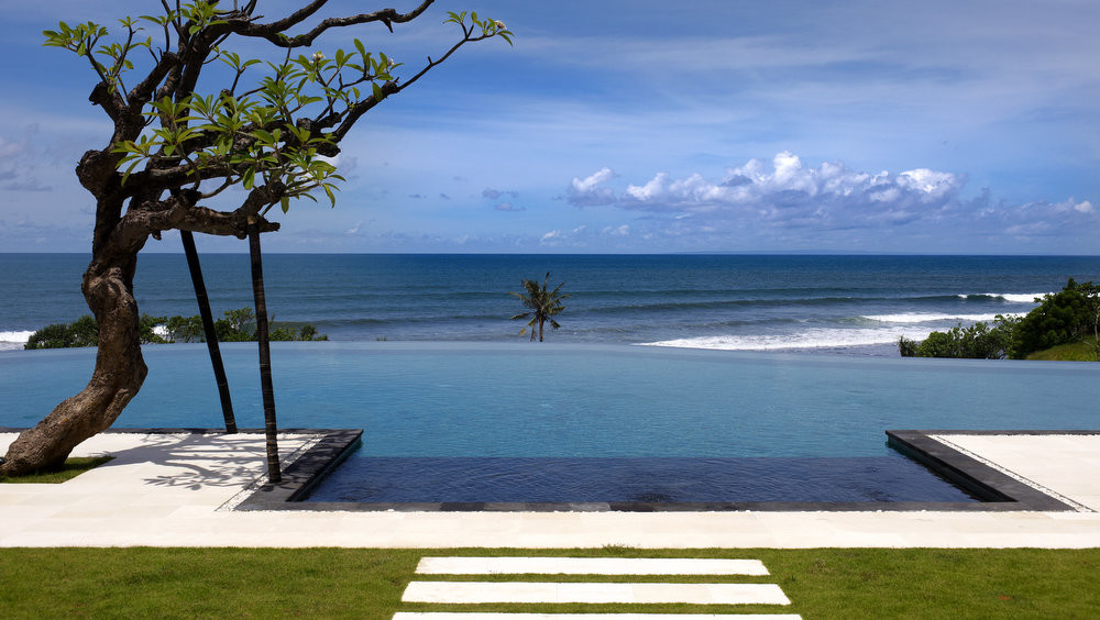 Villa Babar's ocean-facing infinity pool and lawn on a headland in Tabanan, west Bali, with the Indian Ocean and surf beyond