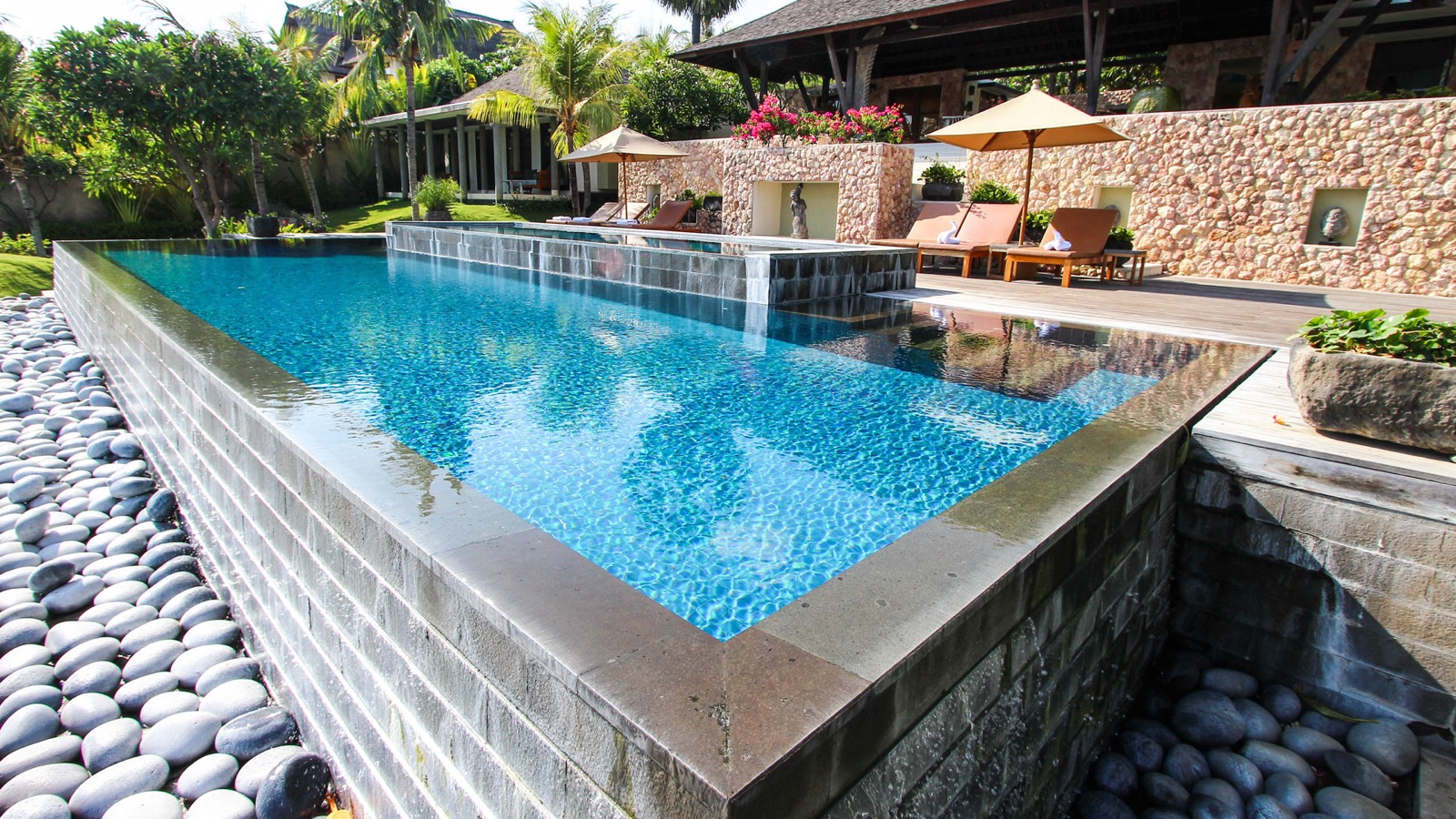 Infinity pool with stone terraces and a thatched pavilion above the shore at Villa Bukit Segara in Amed, east Bali