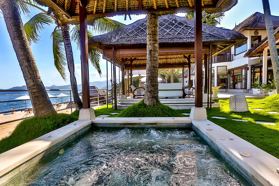 Outdoor jacuzzi under a thatched gazebo at Villa Jukung, with the beach and palms just beyond
