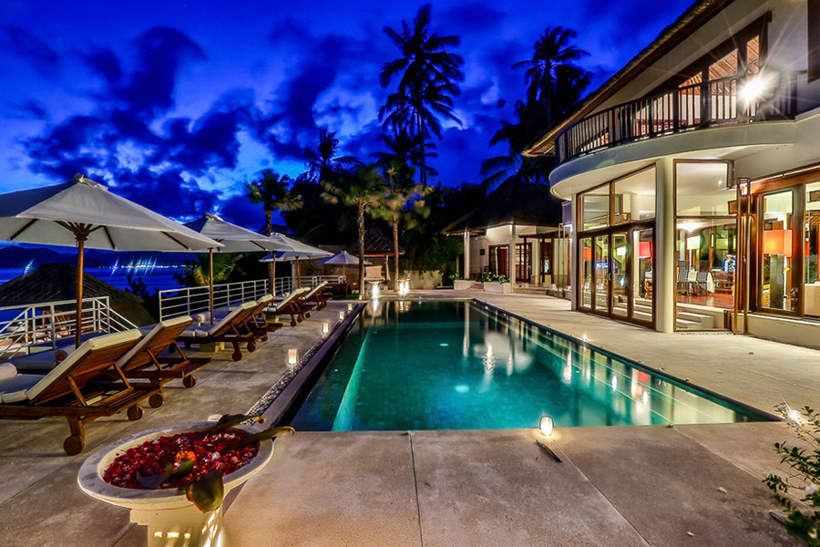 Villa Jukung's swimming pool lit at dusk, running alongside the villa's glass-walled living areas