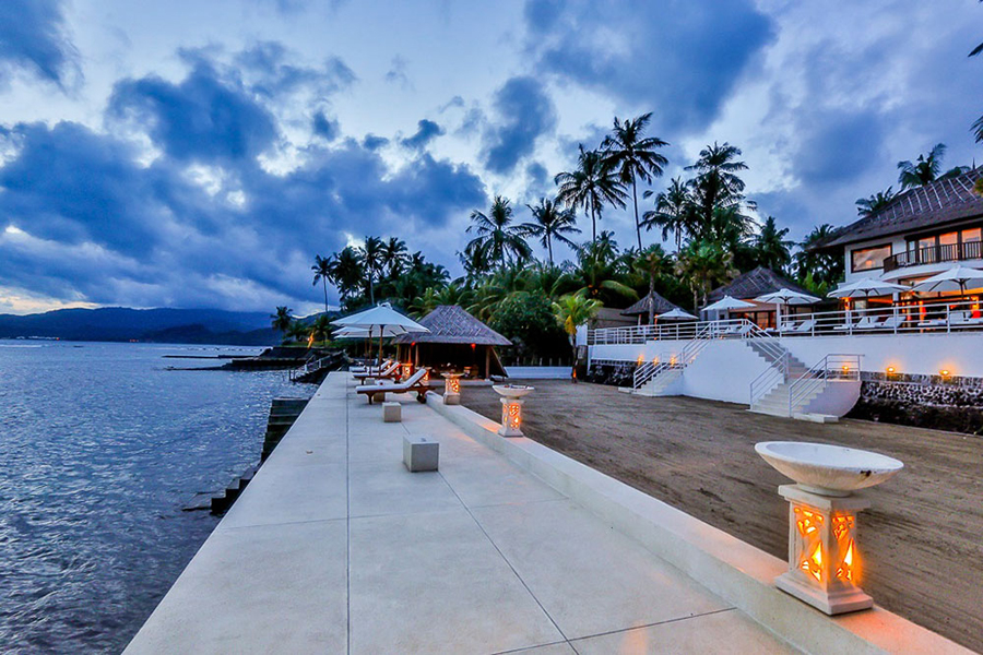 The waterfront deck at Villa Jukung at blue hour, with candle lanterns lining the path to the sea