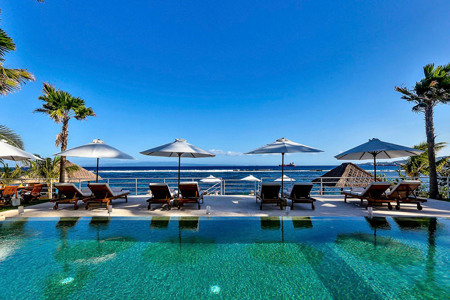 Daytime infinity pool at Villa Jukung in Candidasa, East Bali, with loungers and umbrellas facing the open sea