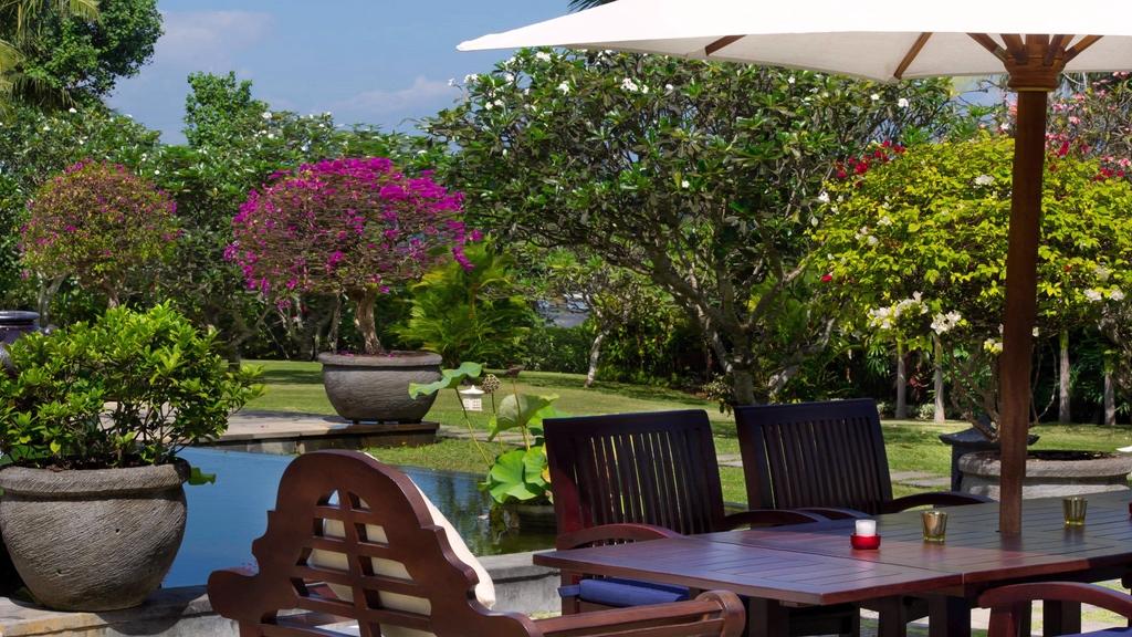 Outdoor dining terrace at Villa Kailasha, shaded by a garden umbrella and flowering trees