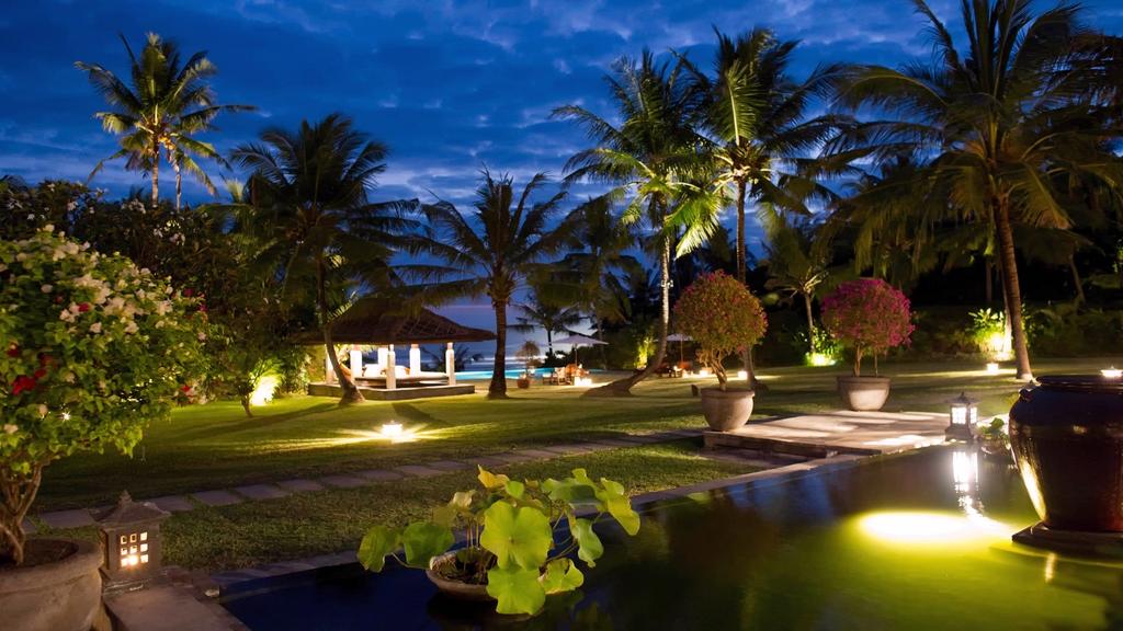 Villa Kailasha gardens and beachfront gazebo lit at dusk, with palm trees and the ocean beyond