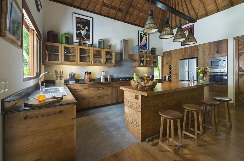 Villa Kavaya's open kitchen with a carved teak island, bar stools and rattan pendant lights