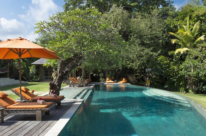 Poolside loungers under orange umbrellas beside a frangipani tree at Villa Kavaya