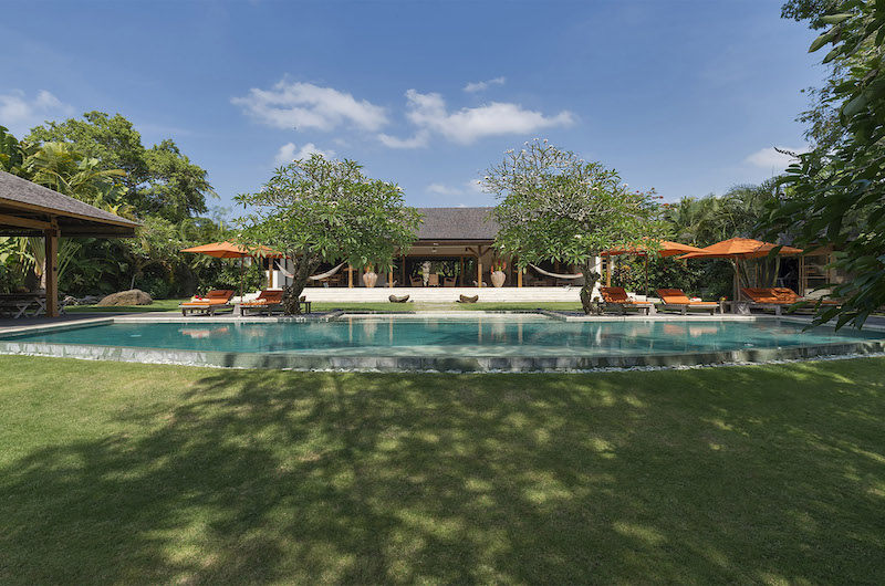 Villa Kavaya's pool and lawn by day, with the open-sided living pavilion and frangipani trees behind