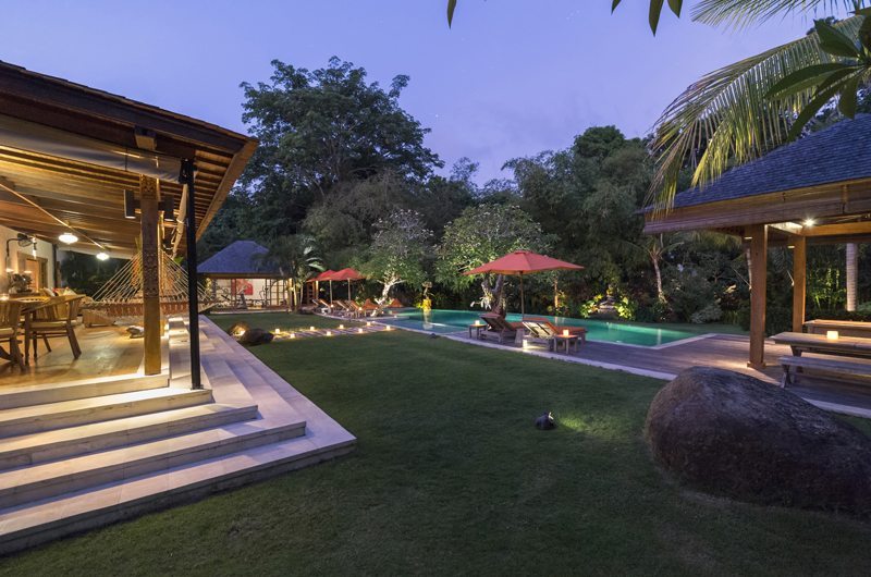 Villa Kavaya's lawn, pool and open living pavilion lit at dusk, framed by tropical garden in Canggu