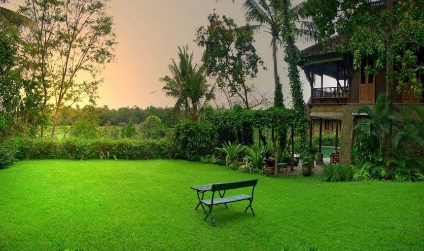 Garden lawn and timber pavilions at Villa Kirana at dusk, with rice fields beyond