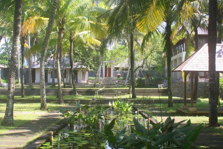 Garden path descending past a lily pond toward Villa Lalang's guest pavilions in the morning light