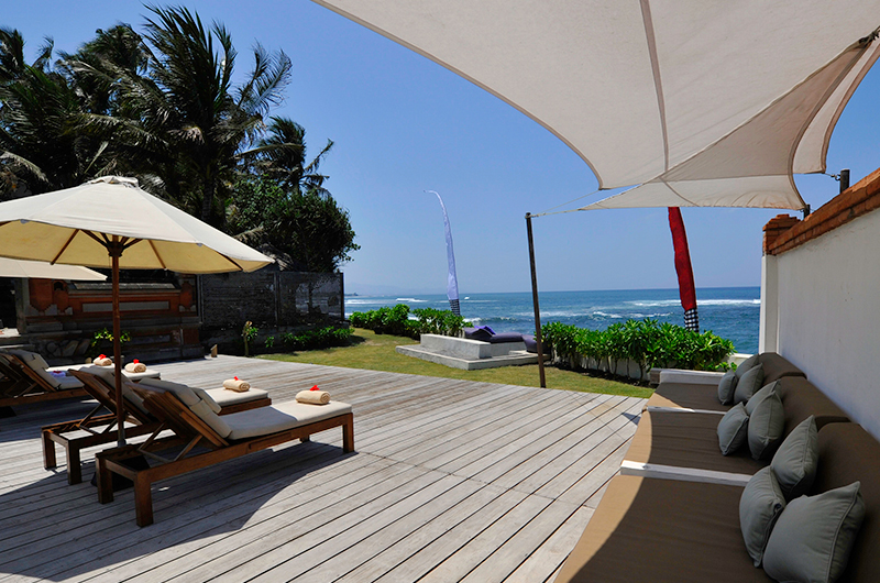 Beachfront timber deck with sun loungers and a sail shade looking out to the ocean at Villa Maya, Majapahit Beach Villas