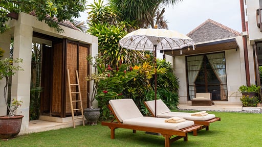Sun loungers on the lawn beside the villa's garden pavilions at Villa Majapahit Nataraja