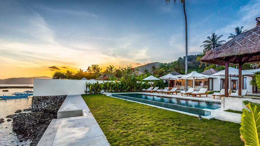Villa Oceana's seawall, pool, and moored boats at sunset on the Candidasa waterfront